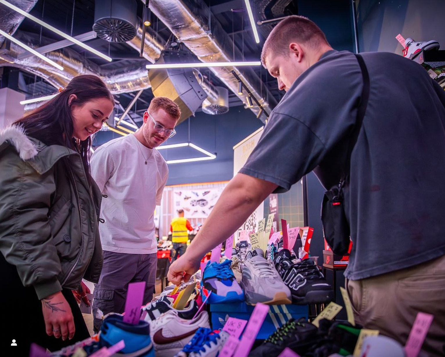 Three people shopping for shoes in a store with a focus on the shoe display.